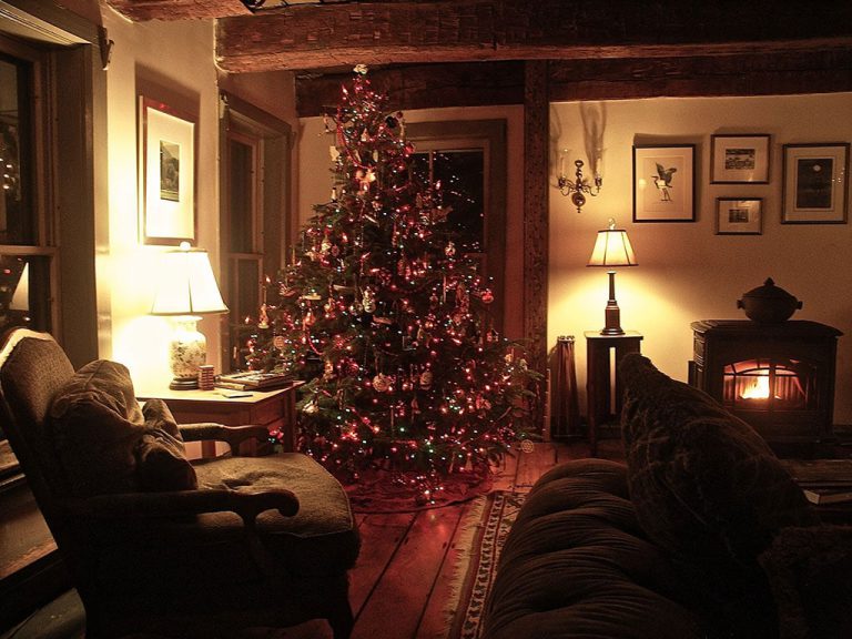 Living room of the inn with lit Christmas tree, plush chair and sofa and a fire burning in the wood stove