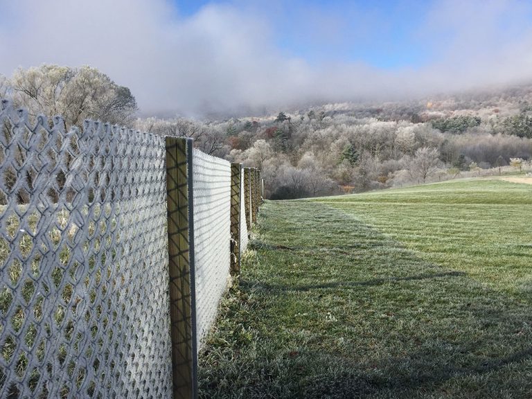 View of a frost-covered fence and frost covered grass and trees