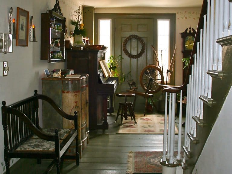 Foyer of the inn with upright piano, green, wooden floors and wooden bench. Stairs up are on the right