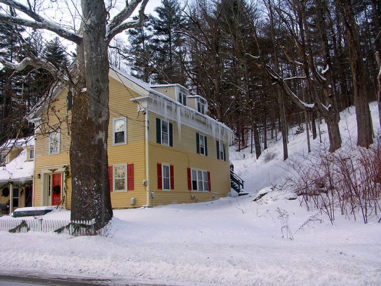 The Ira Allen House Bed and Breakfast, a large yellow house with orange shutters, in the winter with snow and icicles
